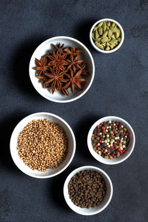 Spices assorted multicolor peppercorns, cardamom, star anise, cumin, coriander, caraway in bowls on black background.の写真素材