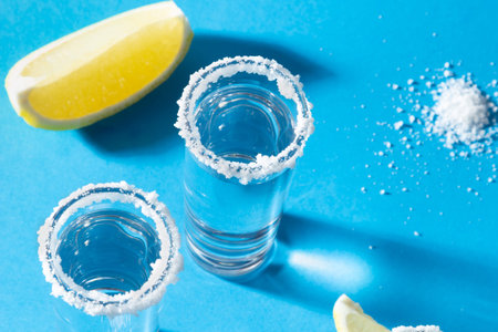 Shots glass of tequila for two persons on blue background with salt and lemon. Concept party. Close upの写真素材