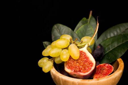 Fresh figs in a wooden plate, with grapes and leaves, shot low key. Vintage, close-up, top view.の写真素材