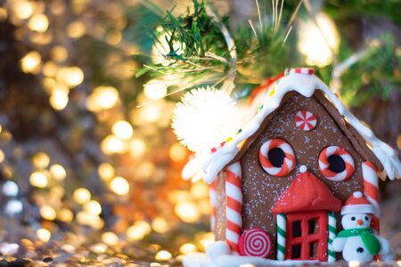Homemade Christmas Gingerbread House displayed on a table. Christmas tree lights in the background.