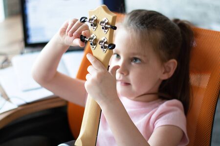 Adorable asian little girl is trying to play ukulele with fully happiness moment, concept of music...