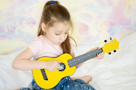 Adorable asian little girl is trying to play ukulele with fully happiness moment, concept of music learning activity for kid development.の写真素材