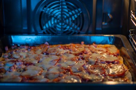 Pizza cooking on a round tray in a gas oven. Pizza with cheese on a round tray Homemade.の写真素材