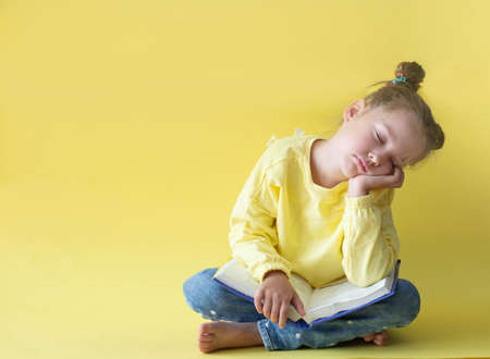 funny child girl yellow jacket on a yellow background, sitting, reading a book, the concept of development and school, back to schoolの写真素材