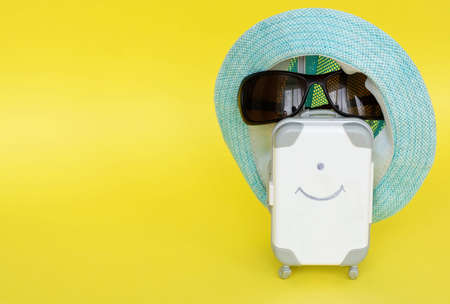white toy suitcase on a yellow background. the concept of travel. space for text, glasses and a blue hat on the suitcase.の写真素材