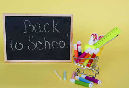 Back to school concept on yellow paper background. Basket with stationery. books. blackboard.