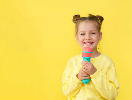 Lifestyle and people concept: a small, happy girl singing with a microphone, isolated by a bright...
