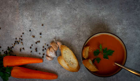 Pumpkin soup in a bowl with crackers, with fresh pumpkins, garlic and parsley, carrots, tomatoes, on a dark background.の写真素材