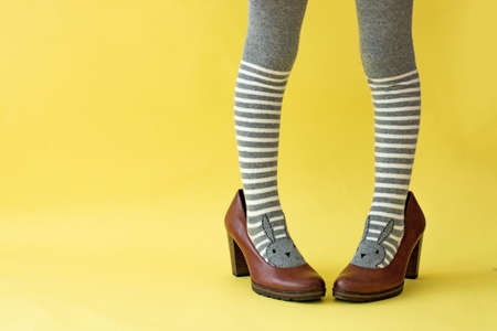 childrens feet in striped tights in adult shoes, on a yellow background.の写真素材