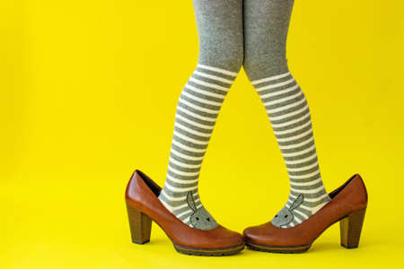 childrens feet in striped tights in adult shoes, on a yellow background.の写真素材