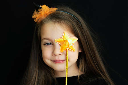 Happy Halloween. Close-up portrait of a happy little girl in a black witch hat on a black background. Childrens Halloween costume. Empty space for text. Layout and copy space.の写真素材