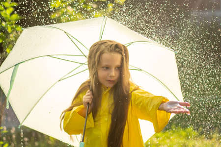 A happy girl with a green umbrella under the summer rain. The girl is dressed in a yellow raincoat...