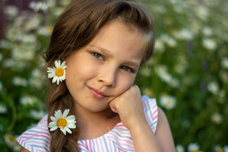 Portrait of a happy little girl with a bouquet of field daisies on a summer day at sunset.の写真素材