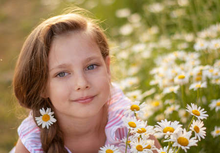 Portrait of a happy little girl with a bouquet of field daisies on a summer day at sunset.の写真素材
