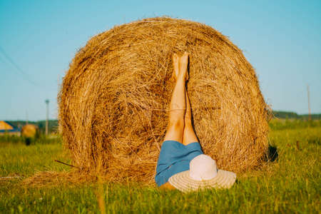 a girl in a hat, in a field, lies near a haystack, putting her feet on itの写真素材