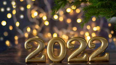 Happy New Year 2022. Golden numbers stand on a fashionable blue background with a backlit bokeh in the background and with a sprig of spruce.の写真素材