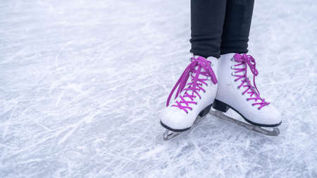Legs of a girl in white figure skates with purple laces on an outdoor skating rink in the park.の写真素材