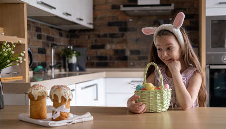 A beautiful child in a bandage with bunny ears, with colorful eggs in a basket, at home in the...