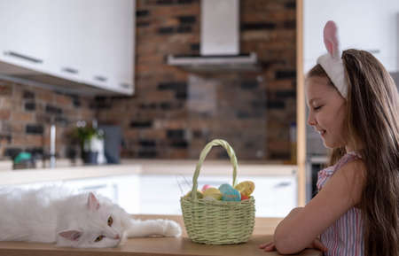A beautiful child in a bandage with bunny ears, with colorful eggs in a basket, at home in the...
