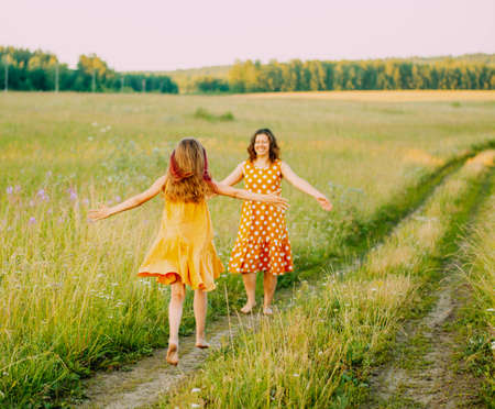 A young mother with her teenage daughter dressed in an orange polka dot dress, having fun in a field outside the city. The concept of Motherhood and childhood.の写真素材