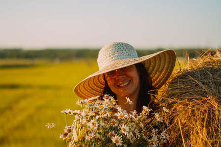Photo of a joyful attractive woman, in an orange polka dot sundress, against the background of a sunset summer evening in a field in flowers.の写真素材