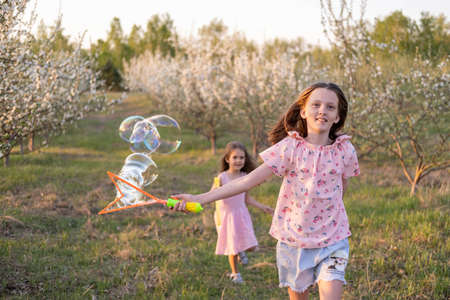 two Caucasian girls are playing in the park with soap bubbles, enjoying a warm sunny day. Summer...