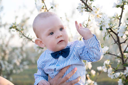 An open portrait of a toddler boy in a cap, a blue shirt with a bow tie, playing in a sunny summer park with his mother, a childs lifestyle. Summer walks with the family.の写真素材