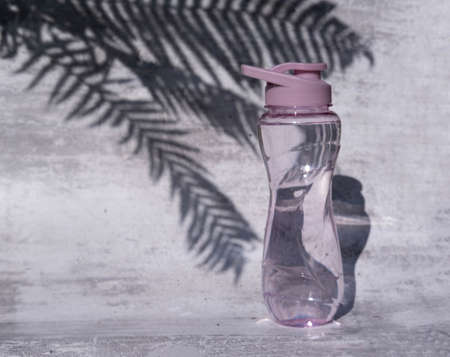 A flat shot of a plastic reusable bottle with an isotonic drink on a gray concrete background with a shadow from palm leaves, hard shadows from the sun, a place to copy.の写真素材