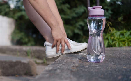 The concept of drinking water. The legs of a woman in white sneakers next to a bottle of water, in a...