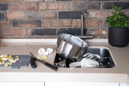A pile of dirty dishes in a metal sink, in the kitchen, against a brick wall.の写真素材