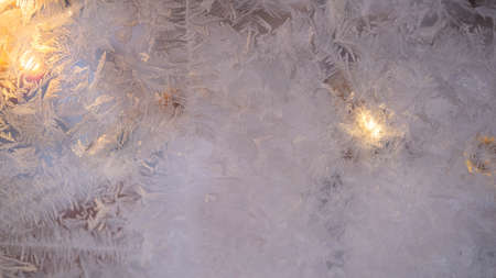 Abstract winter background of frozen glass, through which the lights of the garland glow....