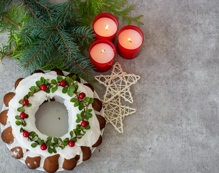Chocolate, cream New Years cake decorated with white cream, green leaves and red berries. A cake on a gray background, with spruce branches and candles. Christmas cake. New Years dessertの写真素材