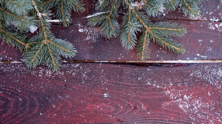 Christmas card. Fir branches decorated with a glowing garland on a maroon wooden background. Border...