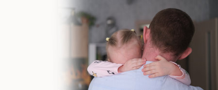 father's day. Close-up of a portrait of a father and his daughter, clinging to his shoulder, and crying. The father cradles and comforts his little daughter.の写真素材