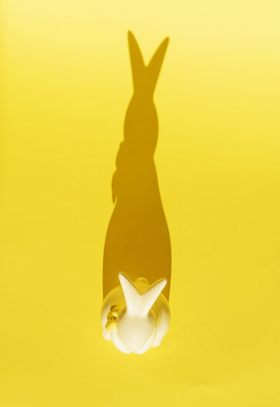 creative photo. Ceramic Easter bunny on a yellow monochrome background, the shadow of a rabbit silhouette, a modern concept and decoration for Easter. Space for copyingの写真素材