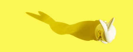 creative photo. Ceramic Easter bunny on a yellow monochrome background, the shadow of a rabbit silhouette, a modern concept and decoration for Easter. Space for copyingの写真素材
