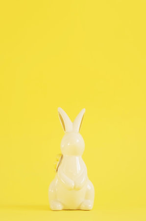 Easter white ceramic rabbit on a yellow background. Festive spring background, happy Easter holidays concept or greeting card.の写真素材