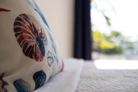 A pillow with a shell print on the bed in the hotel, next to a window with a view of the rainforest,...