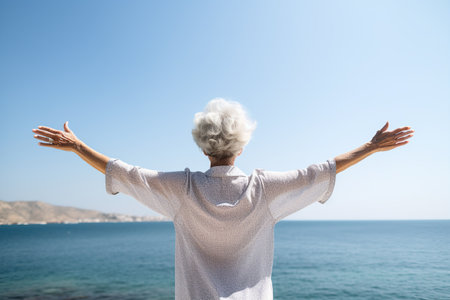 An elderly happy woman stands with her back to the camera against the background of the sea with her arms outstretched. Relaxation and happiness in harmony with yourself.の素材