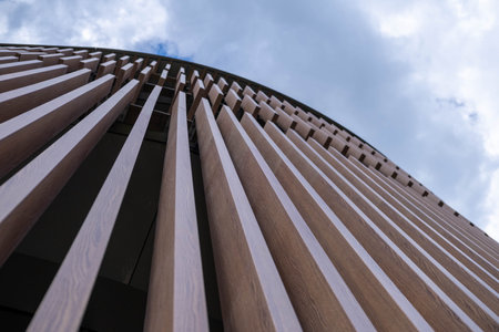 Architectural design featuring wooden slats curving upward against a cloudy sky, showcasing modern...