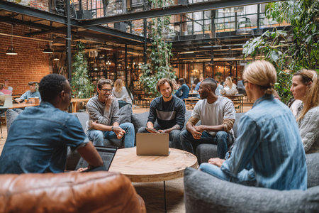 Diverse group of people collaborating around a laptop in a stylish cafe, surrounded by greenery and a warm ambiance, emphasizing teamwork and creativityの素材