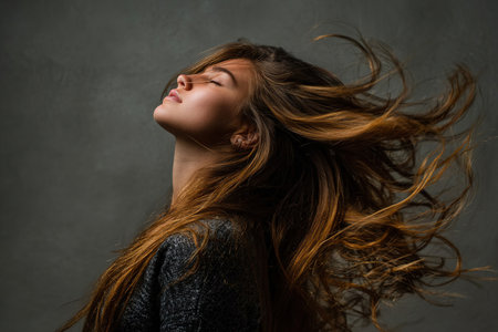 Female model with long hair tilts head back against a textured backdrop, creating a sense of freedom and movement in a captivating portrait that highlights beautyの素材