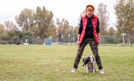 Female dog owner engages with her pet in a grassy park, surrounded by trees and open space, highlighting the bond between them and the joy of outdoor activitiesの写真素材