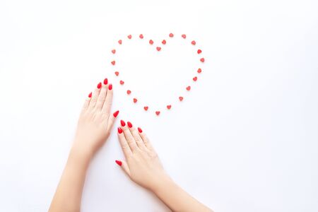 Red manicure on gentle female hands. Hands of a beautiful young woman on a white background and a heart-shaped pattern.の写真素材