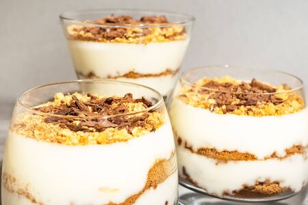 Classic tiramisu dessert in a glass on a gray wooden background. Brightly lit chocolate cake in the...