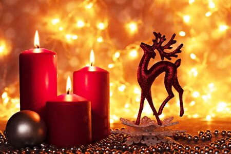 Christmas mood, background with a deer on a white snowflake, burning candles and balls and beads. By the light of bright lights and bokeh.の写真素材