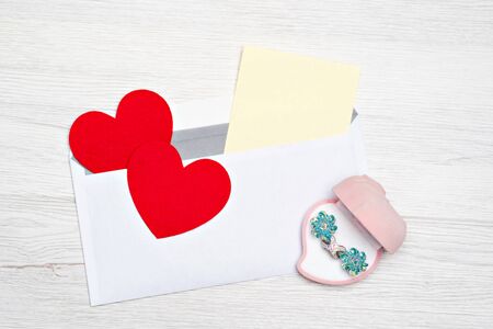 Gift box with jewelry on Valentines Day with an envelope and an attached white sheet for writing on a light background. Two hearts on the feast of St. Valentine.の写真素材