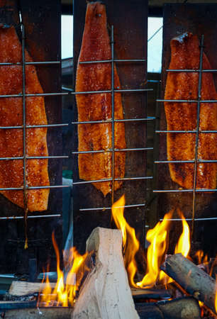 Fish BBQ. Pieces of salmon are fried over an open fire. Fire and smoke envelop the pieces of fish