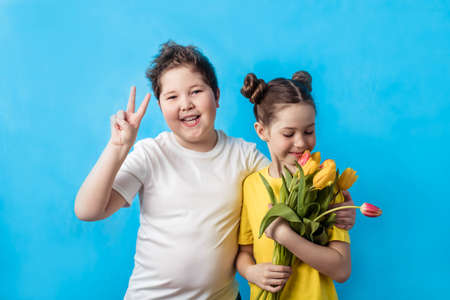 A little boy with a girl and a bouquet of tulips smile happily on a blue background, copy spaceの写真素材