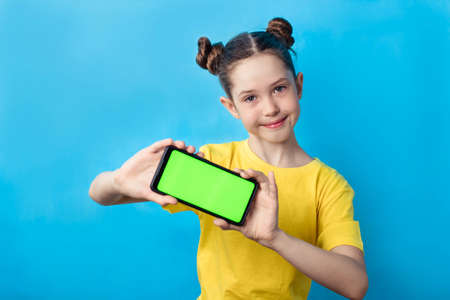 smiling little girl showing smartphone with blank green screen, display mockup for advertising text.の写真素材